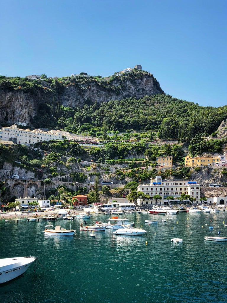 Elegant wooden boat cruising along dramatic cliffs of Amalfi Coast, crystal blue Mediterranean waters beneath historic coastal villas