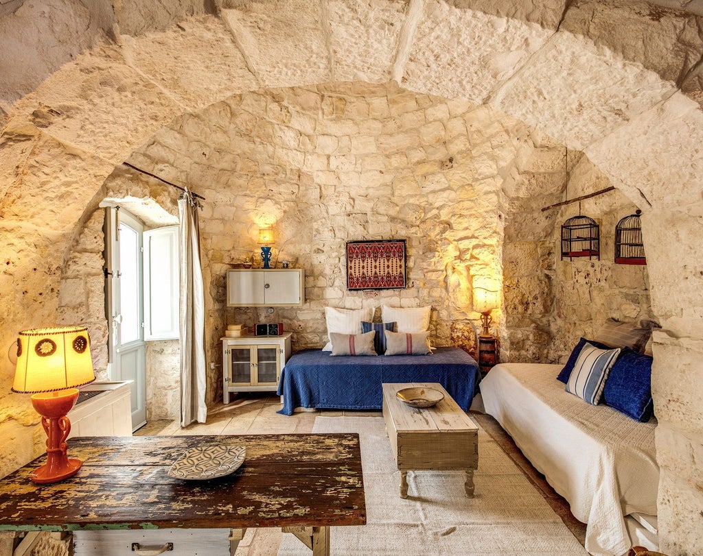 Elegant rustic Italian junior suite with stone walls, wooden furnishings, and soft white linens, showcasing traditional Pugliese architectural charm and luxurious comfort.