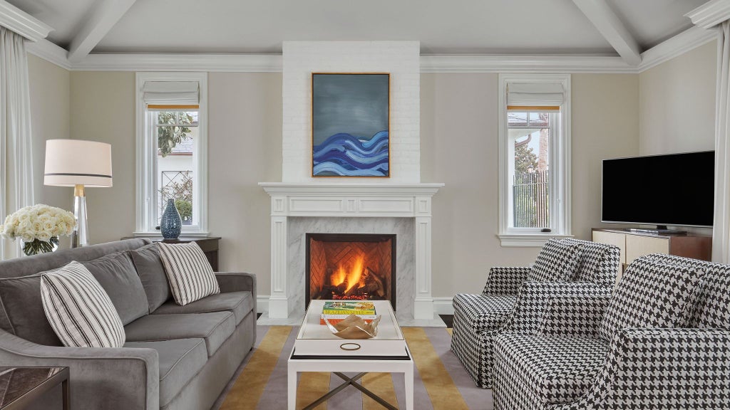 Elegant Montecito bungalow suite with coastal California design, plush white bedding, wood floors, and soft natural light streaming through large windows