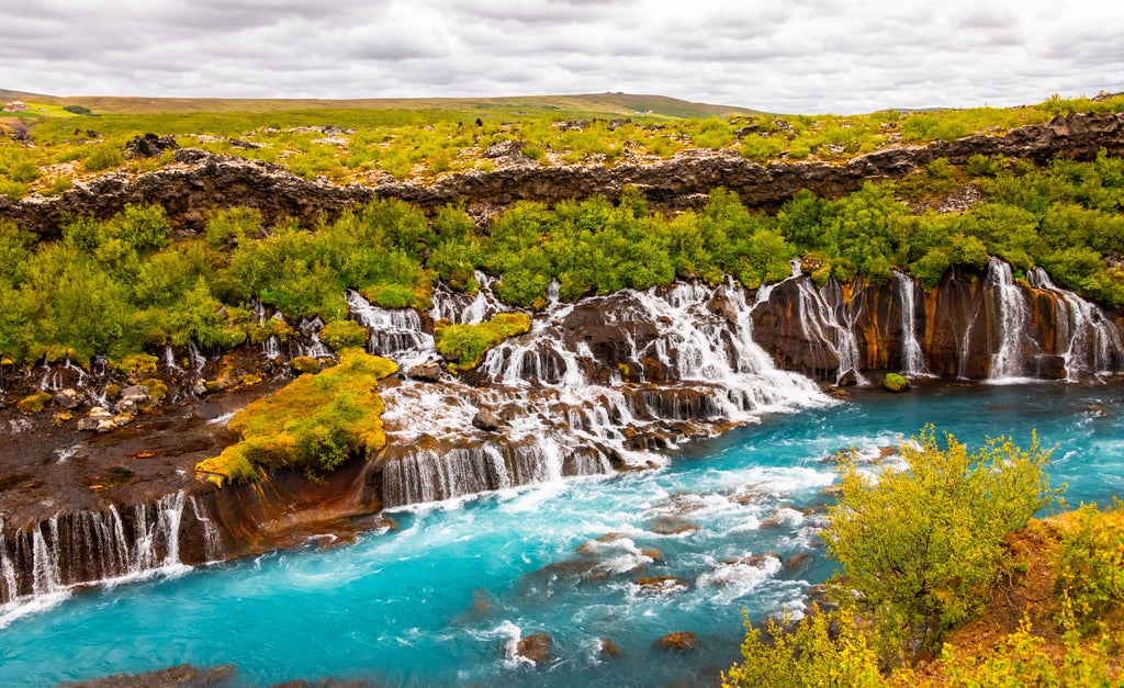 Dramatic Icelandic landscape of Borgarfjörður with verdant green cliffs, cascading waterfalls, and rugged coastal terrain under soft misty lighting