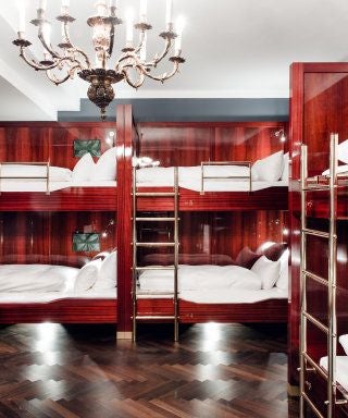 Opulent shared dormitory at Grand Ferdinand hotel, Vienna, with vintage wooden bunk beds, soft ambient lighting, and elegant heritage-style Austrian interior design