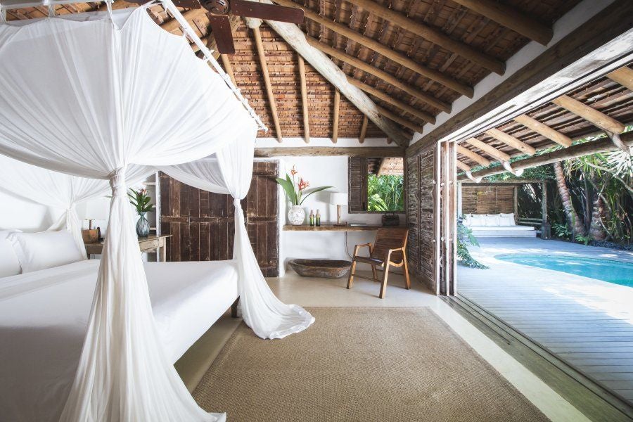 Rustic-chic Brazilian hotel room with wooden furniture, white linens, and tropical coastal decor at eco-luxury resort in Trancoso, Bahia