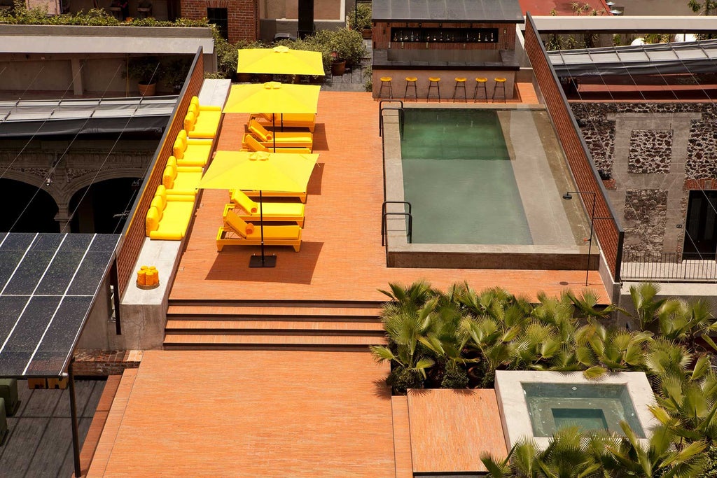 Historic boutique hotel in downtown Mexico City with colonial-style architecture, elegant rooftop terrace overlooking urban landscape and surrounding volcanoes at golden hour