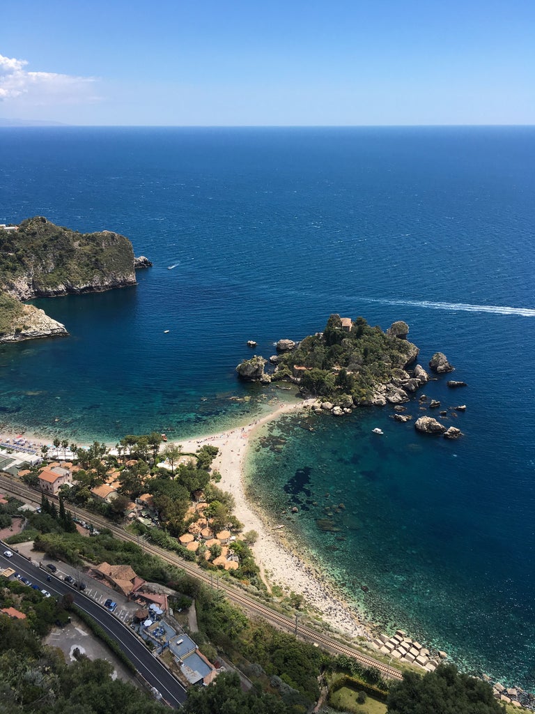 Sun-drenched cliffside town of Taormina, Sicily, with terracotta roofs cascading down to azure Mediterranean waters and Mount Etna looming