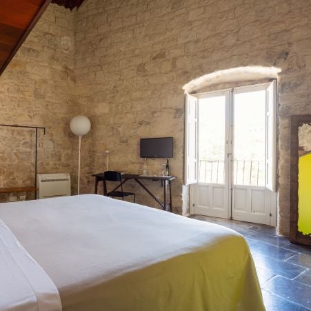 Elegant stone-walled boutique hotel room with rustic wooden furniture, soft linens, and warm Mediterranean light in historic Sicilian setting