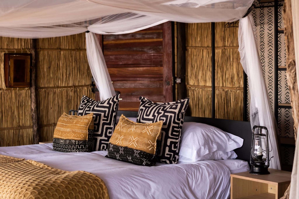 Luxurious safari room with canvas-draped bed, wooden furnishings, and warm ambient lighting overlooking lush wilderness in a remote Zambian wildlife camp