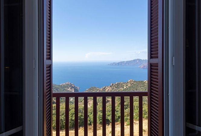 Minimalist seaside hotel room with white linens, Mediterranean blue accents, and expansive ocean view through large windows at Les Roches Rouges