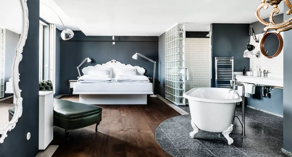 Luxurious Vienna hotel suite with plush white bed, elegant wooden furnishings, large windows overlooking urban landscape, and refined Austrian design aesthetic