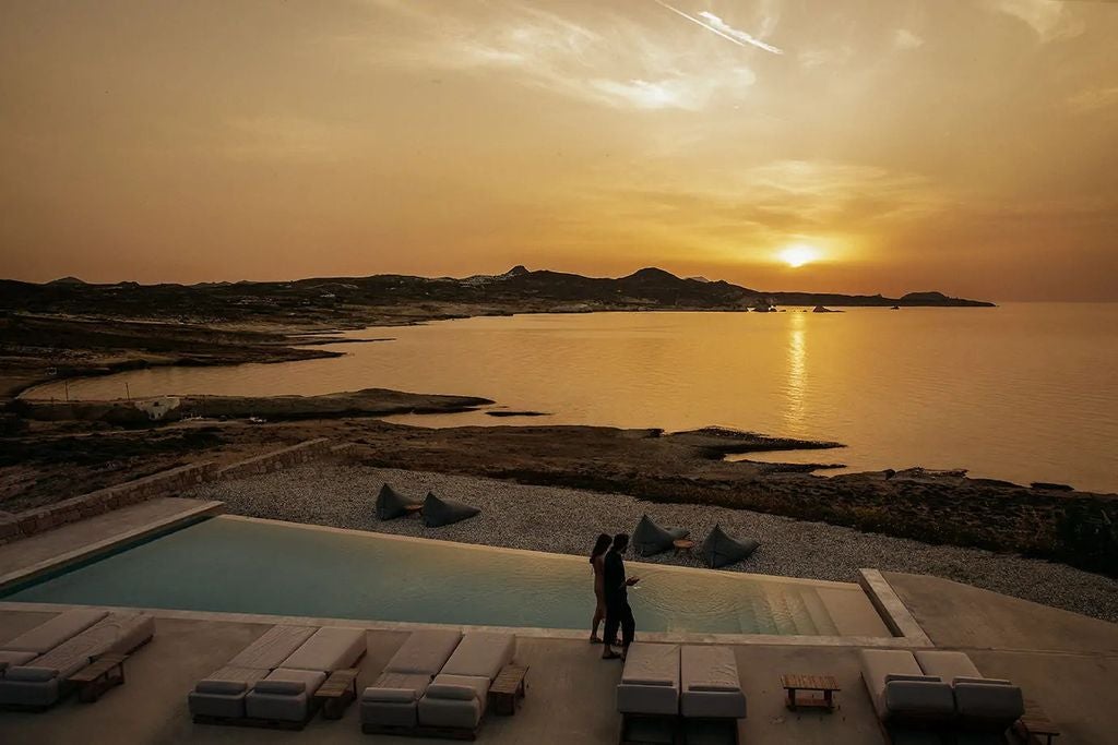 Whitewashed luxury villas with private pools cascade down a hillside overlooking the crystal-blue Aegean Sea in Milos, Greece