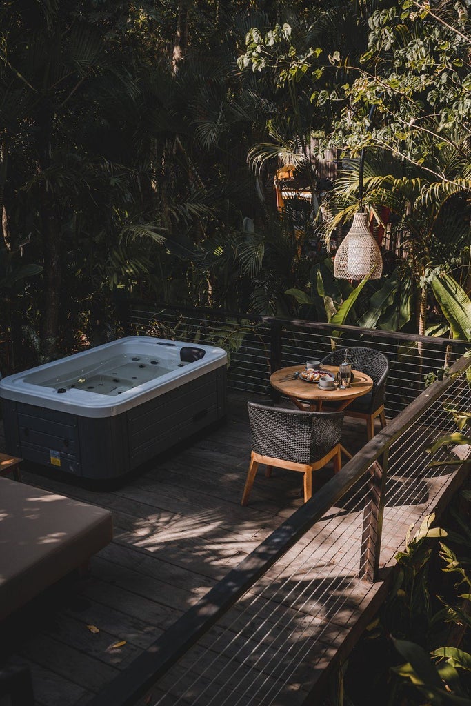 Luxurious wooden cabin suite with glass walls, private outdoor jacuzzi, and panoramic mountain views through lush Indonesian rainforest