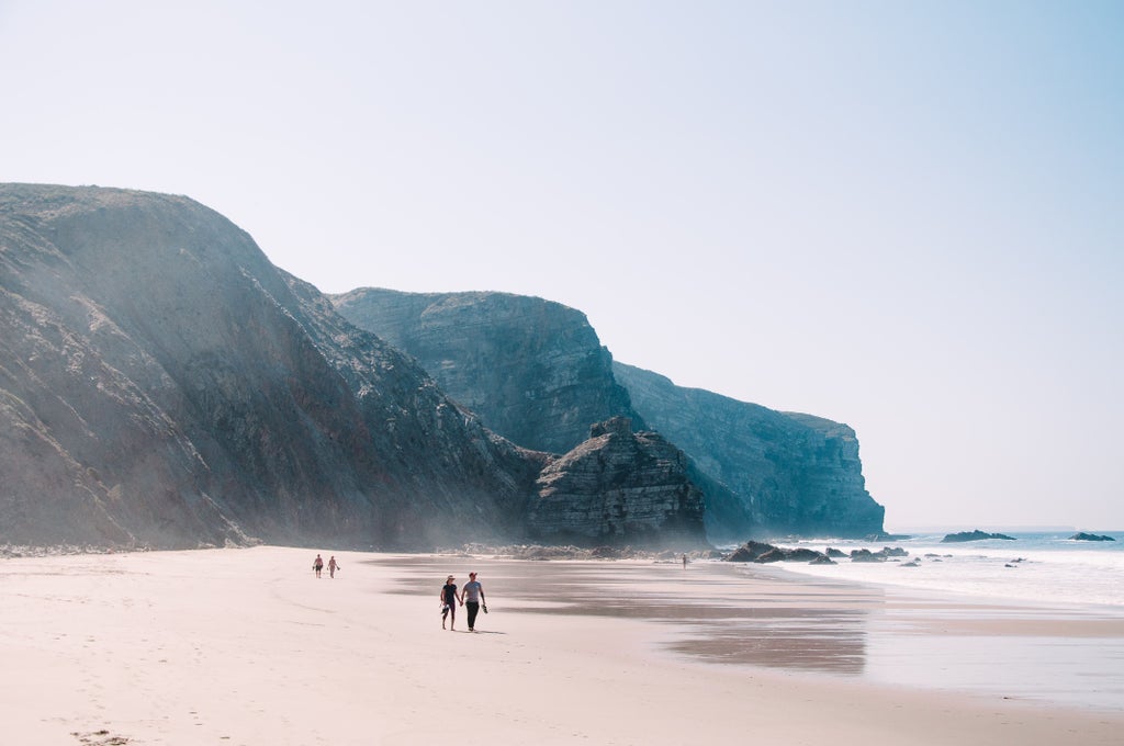 Dramatic cliffside view of pristine sandy beach and turquoise Atlantic waters along Portugal's Algarve coast at golden hour