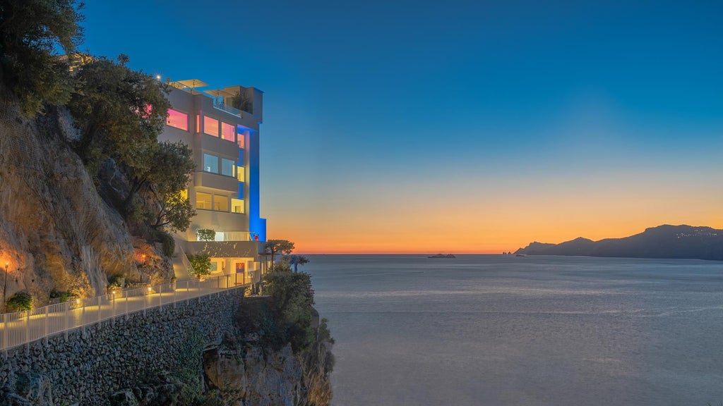 Minimalist white luxury boutique hotel perched on Amalfi Coast cliffs, overlooking azure Mediterranean waters with elegant, clean architectural design