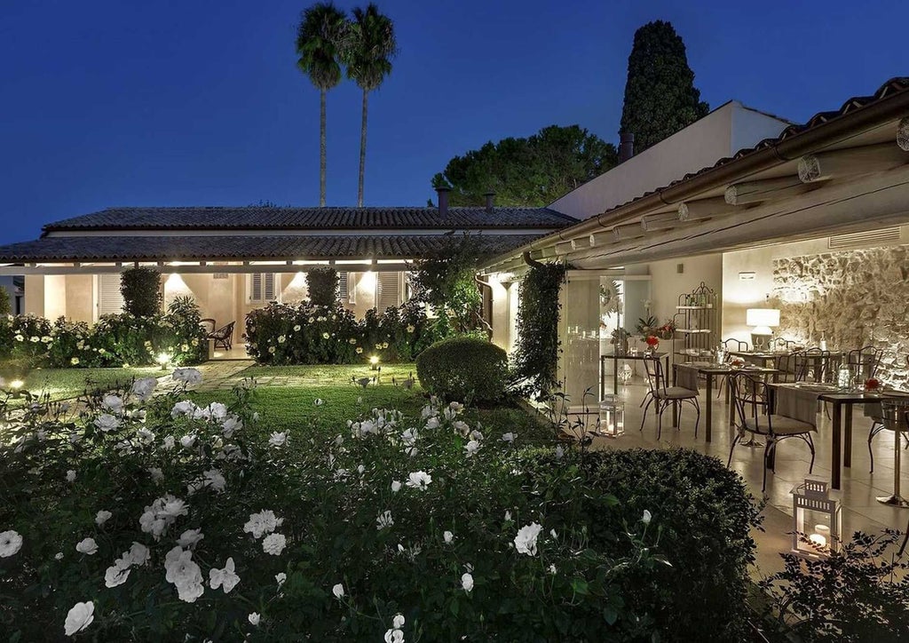 Elegant Sicilian hotel room with soft cream walls, antique wooden furniture, and refined linens at Donna Coraly Resort in Syracuse, showcasing rustic Mediterranean charm