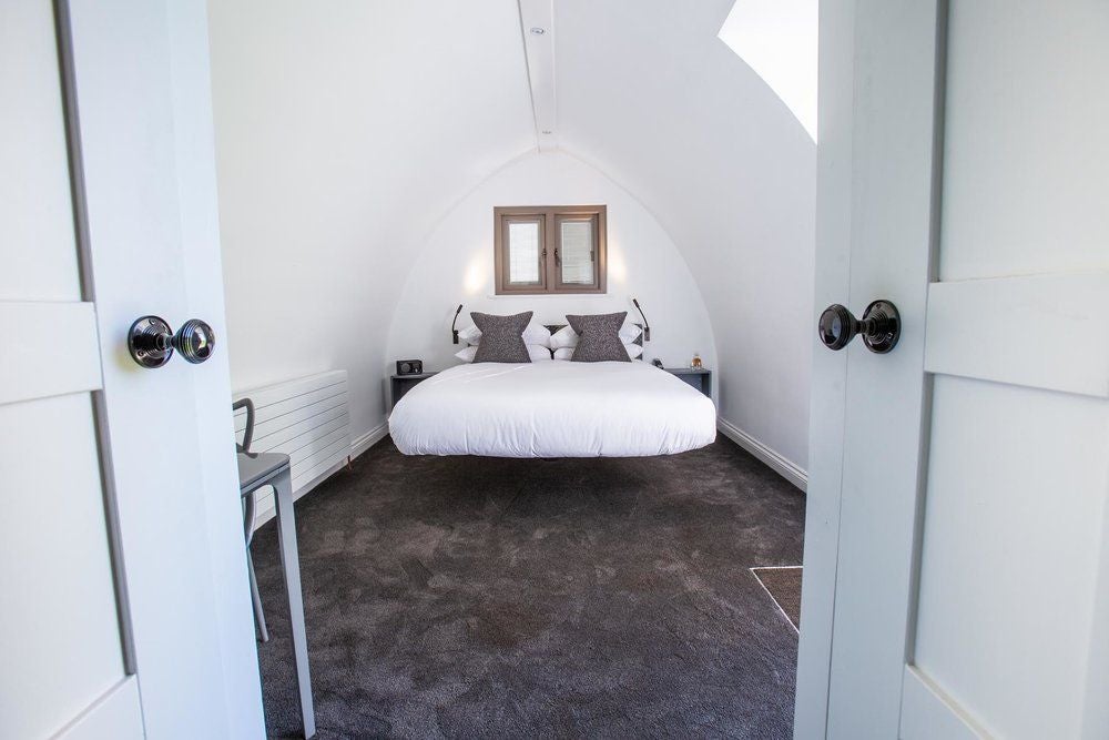 Serene, luxurious hotel room at Tuddenham Mill with elegant wooden furnishings, plush bedding, and soft natural light streaming through large windows.