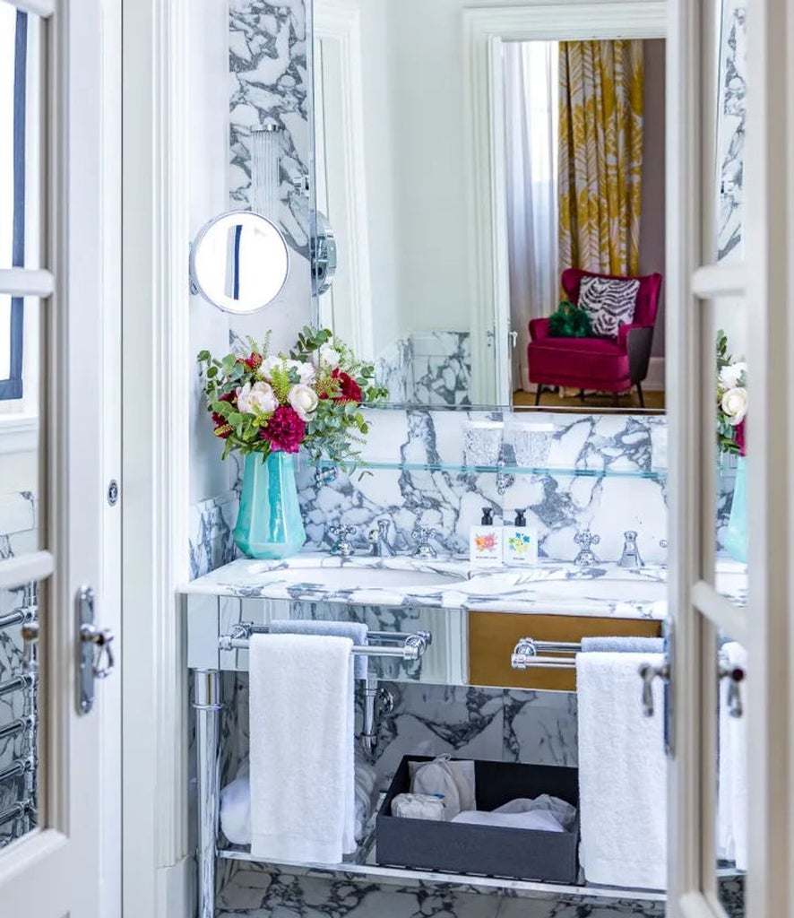 Elegant deluxe hotel room with velvet green headboard, antique-style furnishings, crystal chandelier, and marble bathroom in warm lighting