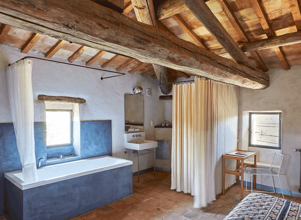 Elegant stone-walled bedroom with rustic wooden furniture, soft white linens, and warm lighting in a luxurious French countryside hotel suite