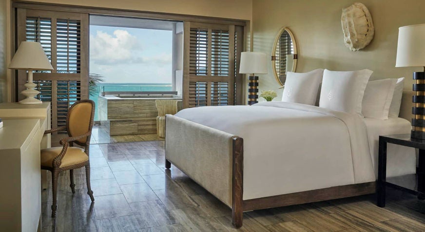 Luxurious ocean-view studio with modern furnishings, king bed, private balcony overlooking Caribbean waters and crisp white decor