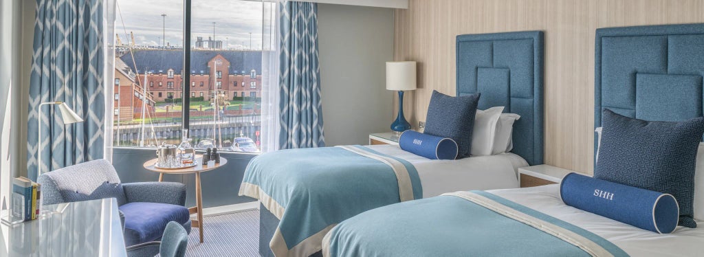 Modern twin hotel room with two comfortable beds, sleek neutral decor, contemporary furnishings, and large window overlooking urban landscape in Harbour Hotel Southampton, United Kingdom