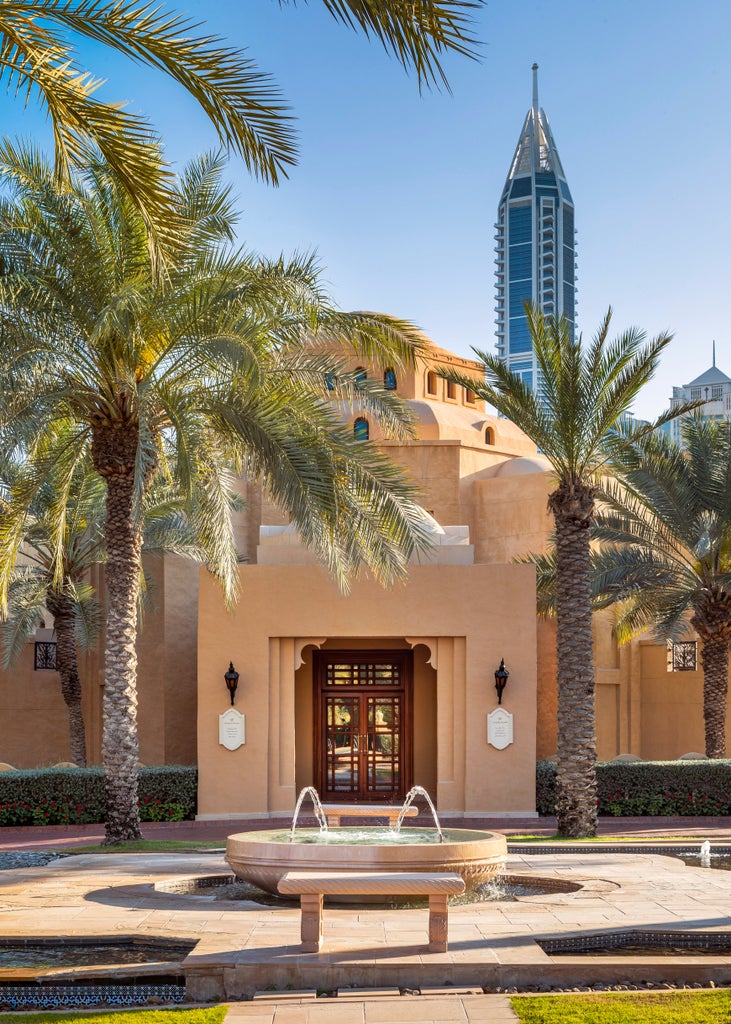 Opulent beachfront hotel with grand Moorish architecture, towering palm trees, and manicured gardens along Dubai's exclusive coast