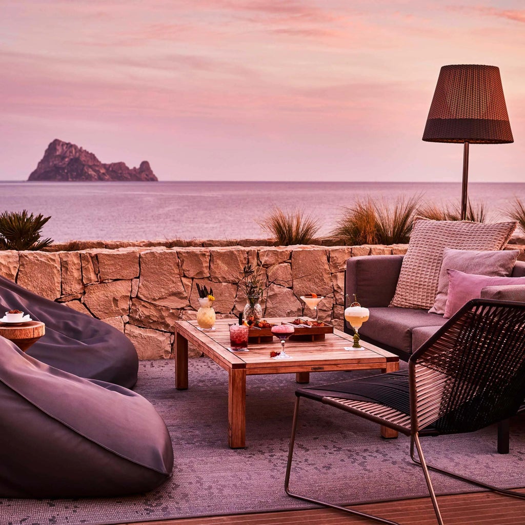 Luxurious white-walled resort nestled on Ibiza's rocky coastline, overlooking azure Mediterranean waters with elegant infinity pool and modern architecture