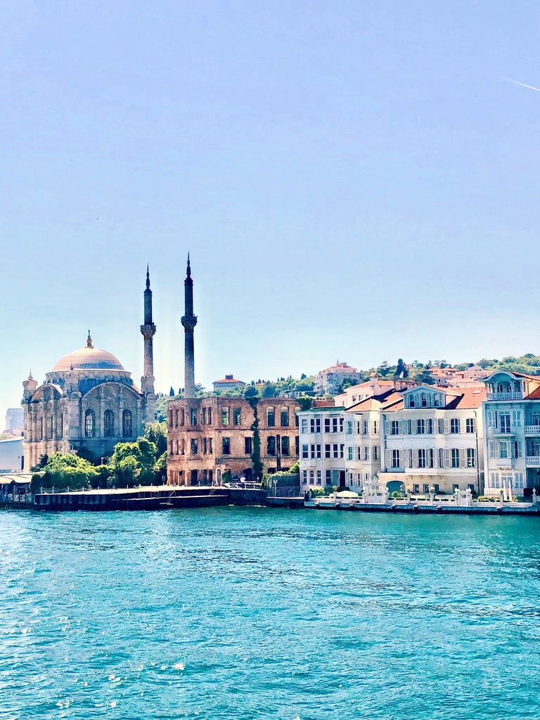 Istanbul's iconic Hagia Sophia at sunset, golden light illuminating its domes and minarets against a warm pink and orange sky over the Bosphorus