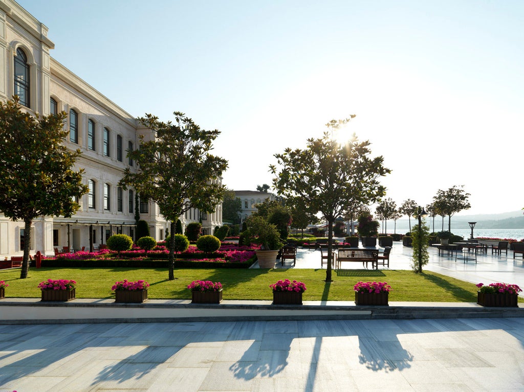 Elegant waterfront hotel with Ottoman-style architecture, marble terraces, and palm trees overlooking the Bosphorus strait at sunset