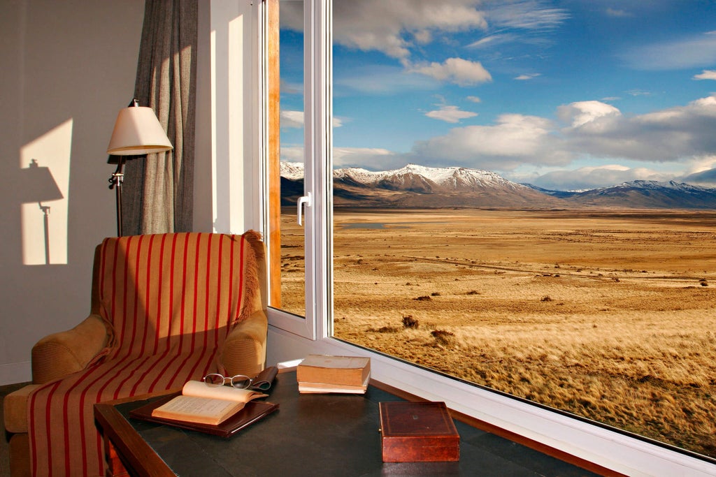 Stone and wood luxury lodge nestled in rugged Patagonian grasslands, with snow-capped mountains and vast plains in background