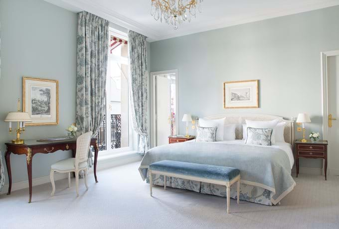 Elegant junior suite at Le Bristol Paris with pale green walls, crystal chandelier, ornate furnishings, and luxurious French windows