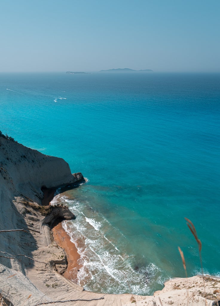 Breathtaking aerial view of Corfu's turquoise coastline, featuring luxury villas nestled among lush hills and a pristine sandy beach