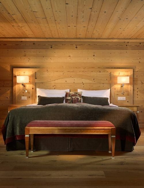 Elegant chalet-style suite with wooden beams, plush queen bed, mountain-view balcony, and refined Swiss Alpine furnishings at Mont Cervin Palace