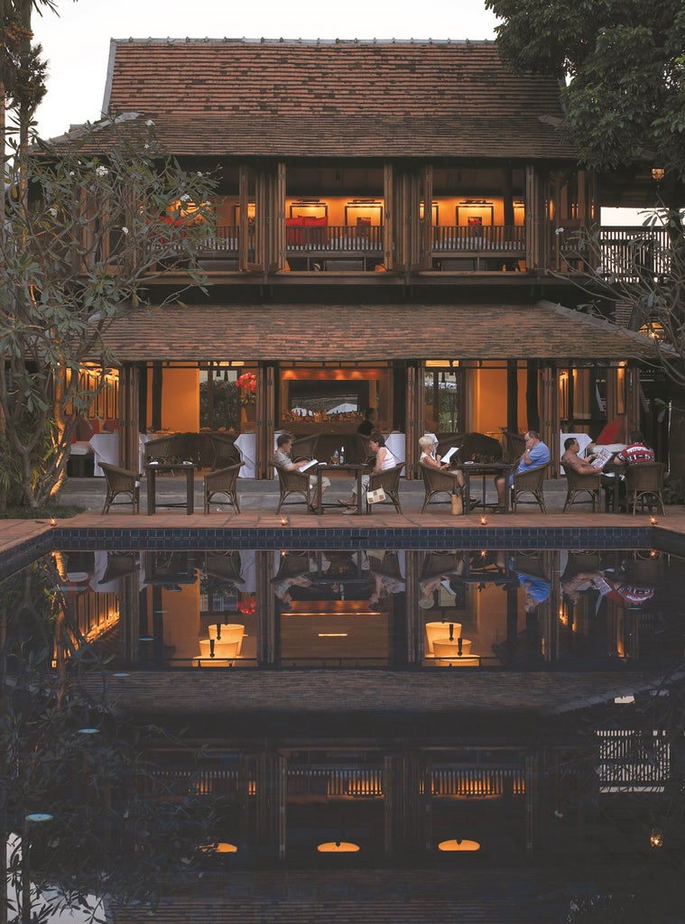 Elegant Thai resort entrance with stone pathway lined by ancient tamarind trees, leading to traditional teak pavilion and lush gardens