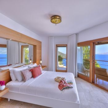 Luxurious standard room at Villa Mahal, featuring elegant white bedding, minimalist decor, and panoramic views of scenic Turkish landscape through large windows.