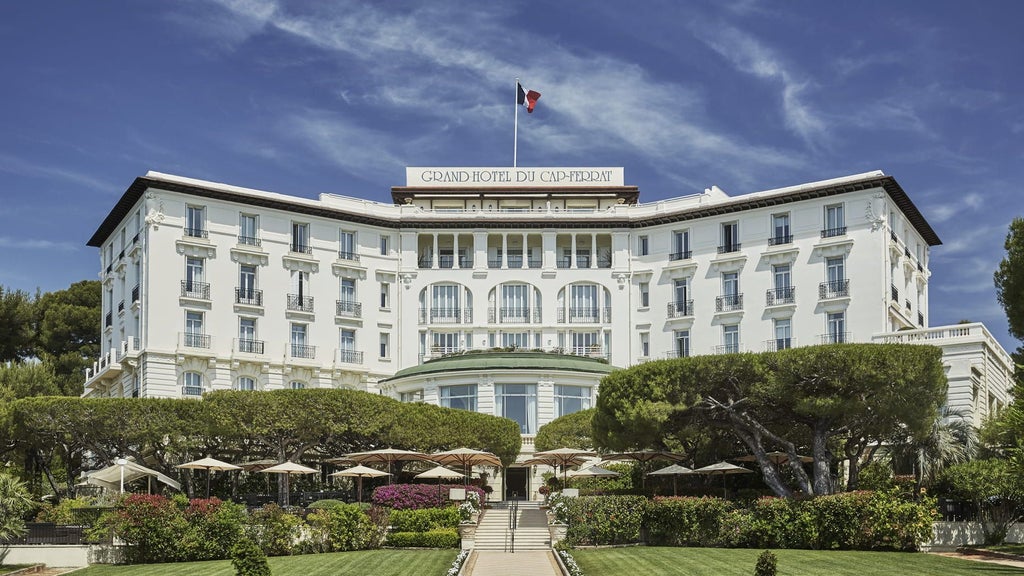 Opulent Mediterranean hotel with pristine white facade overlooking French Riviera coastline, surrounded by manicured gardens and palm trees