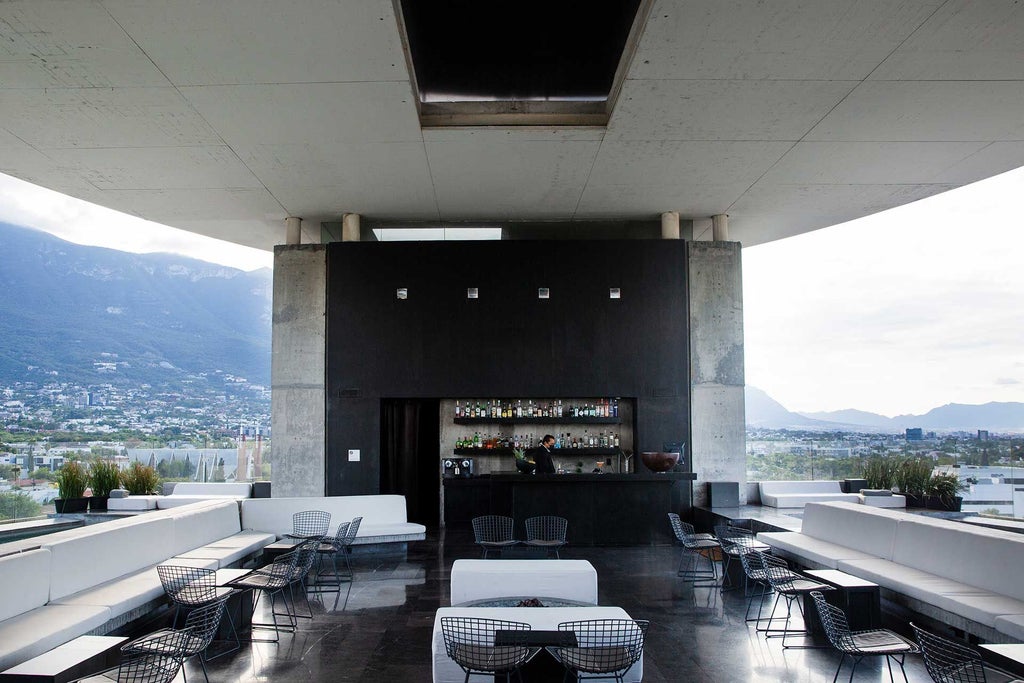 Sleek modernist hotel with glass facade overlooking Monterrey skyline, featuring minimalist architectural design and urban landscape at dusk