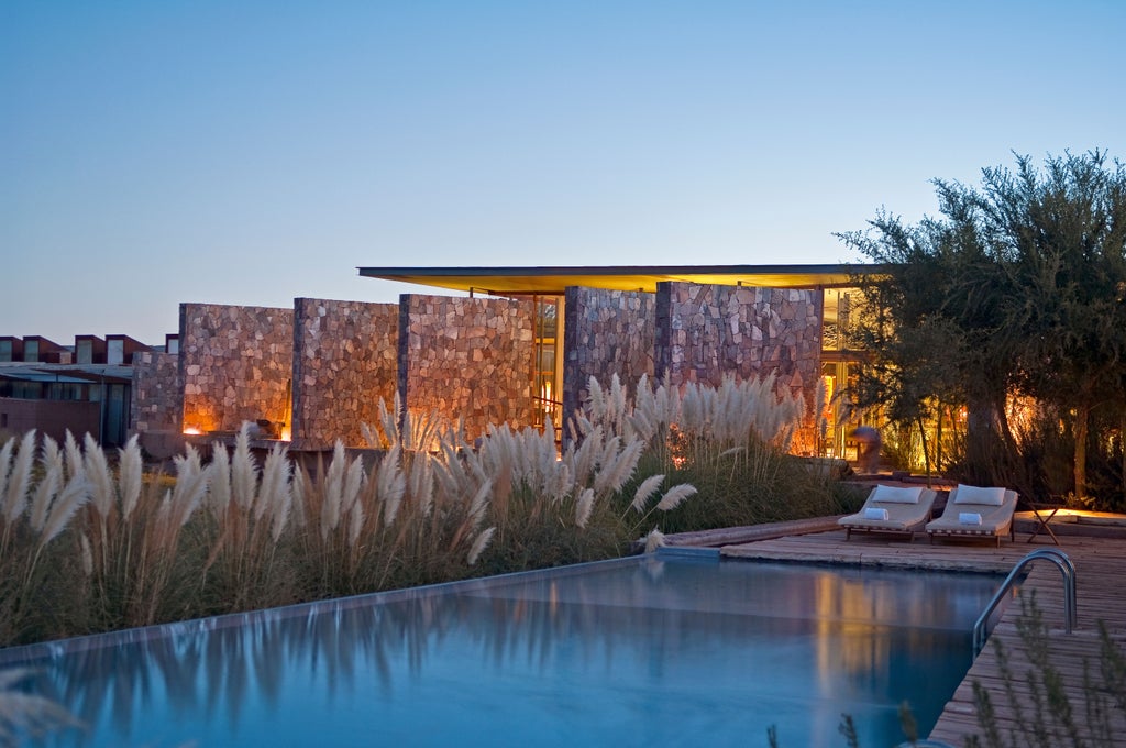 Modern desert resort with infinity pool overlooking Atacama Desert, framed by dramatic Andes Mountains against a clear blue sky