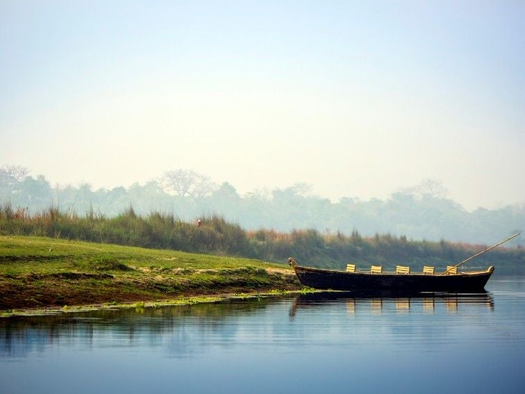 Elegant safari lodge with thatched-roof villas nestled in lush Nepal jungle, overlooking serene river and misty mountain backdrop