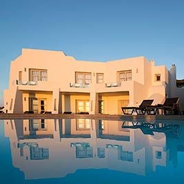 Luxurious seaside resort with white minimalist architecture, infinity pool overlooking azure Aegean waters, and elegant stone terraces at sunset in Greece