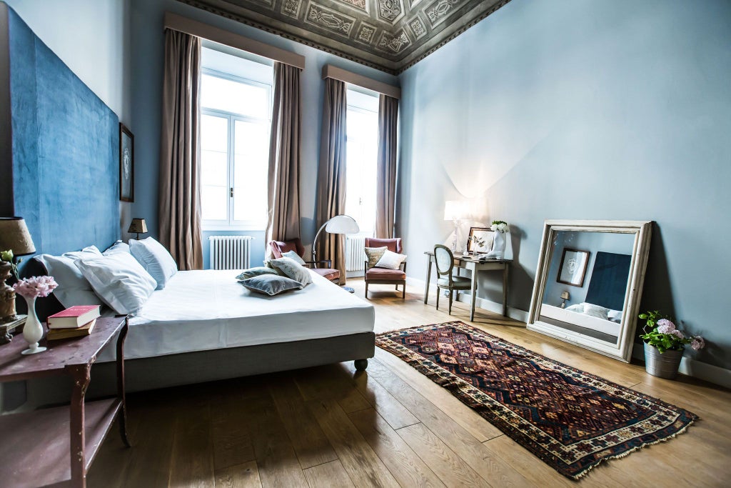 Elegant Tuscan-style deluxe room with vintage furnishings, ornate wooden headboard, and warm neutral tones in a boutique hotel in Florence, Italy