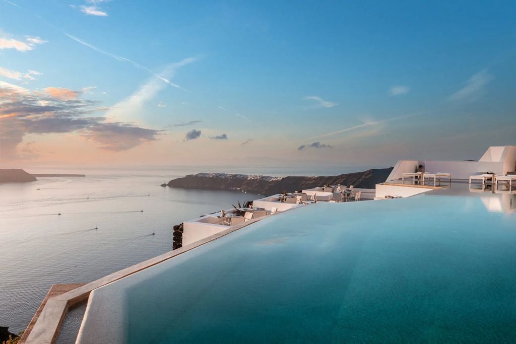 Whitewashed luxury hotel with infinity pool overlooking the Aegean Sea, featuring curved architecture and private terraces at sunset