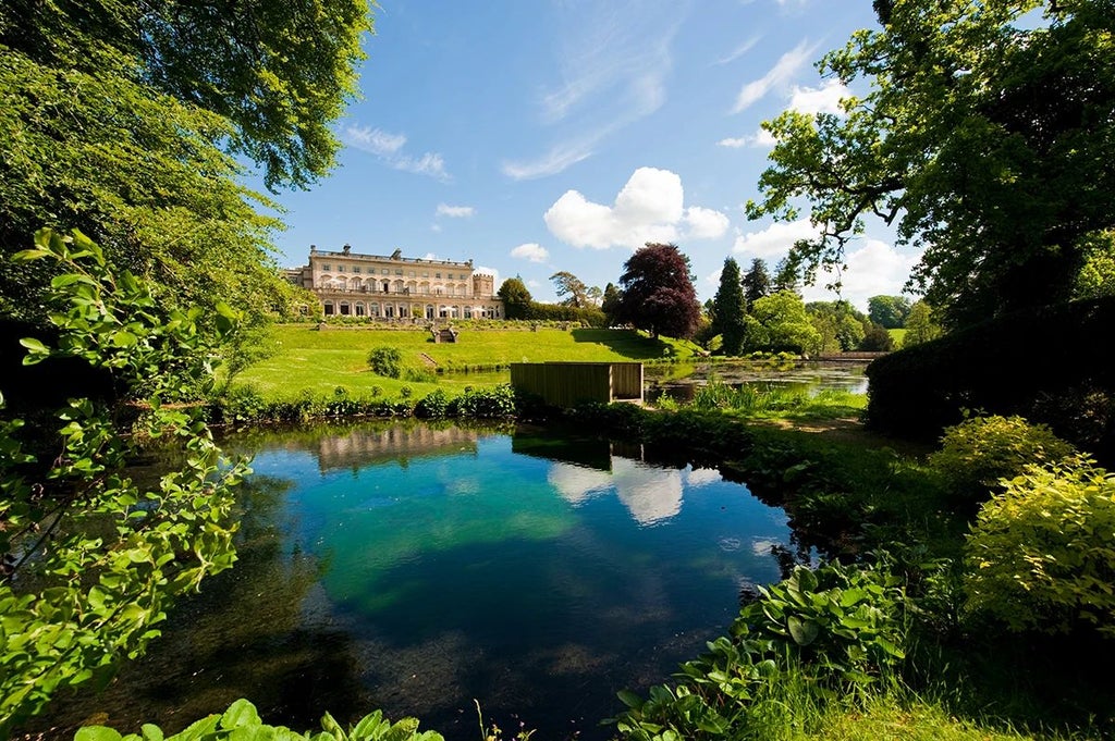 Luxurious countryside manor with modern glass extensions, set against lush green Cotswolds landscape, featuring contemporary design and natural stone architecture.