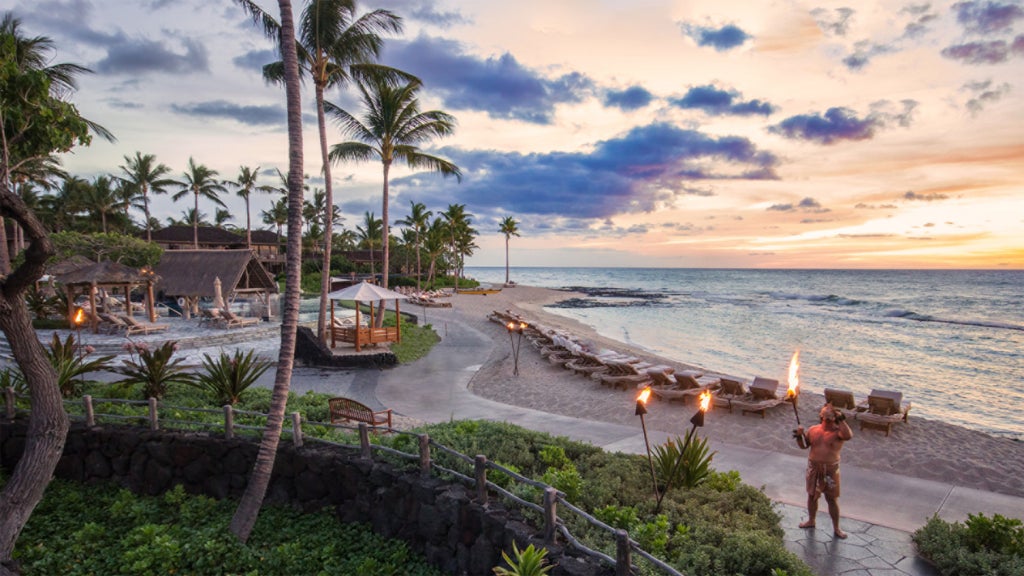 Luxury beachfront resort with infinity pool overlooking Pacific Ocean, palm trees and white loungers at sunset in Hawaiian paradise