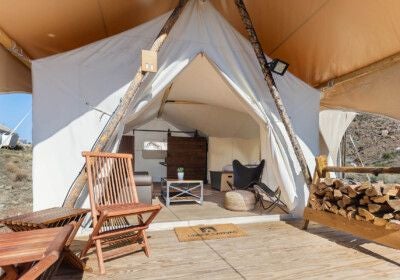 Luxurious glamping suite with king bed, neutral linens, canvas walls, and scenic Zion landscape views through large tent windows.