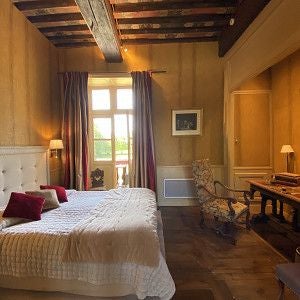 Elegant French château hotel room with ornate antique furniture, rich burgundy draperies, and refined period decor in muted gold and cream tones