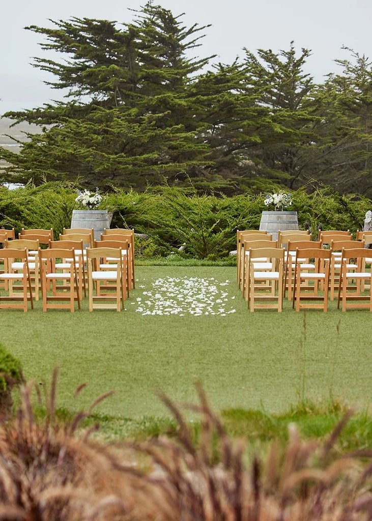 Rustic coastal lodge nestled among cypress trees, featuring weathered wood exterior, ocean view terrace, and warm, inviting lighting at twilight.