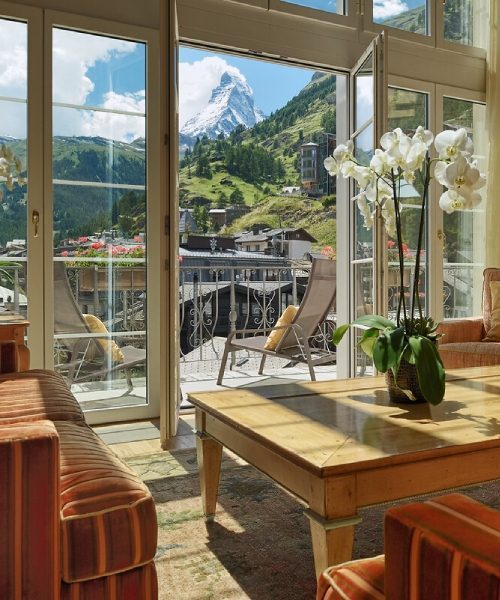 Elegant mountain suite with panoramic Matterhorn views, featuring a plush king bed, crystal chandelier, and classic Swiss alpine decor