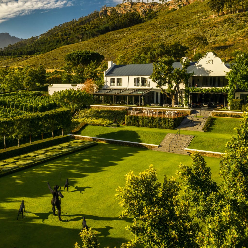 Elegant white Cape Dutch-style manor house with manicured gardens and mountain backdrop at Leeu Estates luxury hotel in South Africa