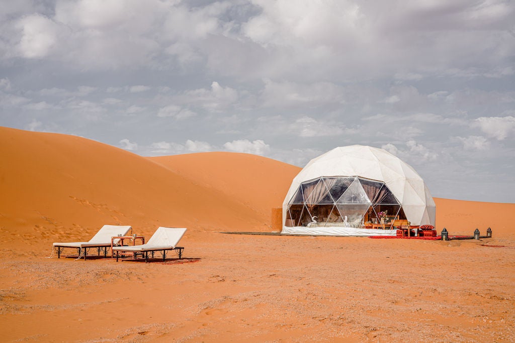 Luxurious Moroccan desert camp featuring elegant white canvas tents against golden sand dunes, traditional rugs and lantern lighting