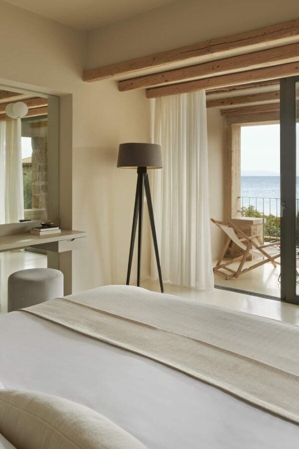 Elegant minimalist hotel room with white decor, wooden accents, and panoramic sea view, embodying luxurious Greek island retreat design