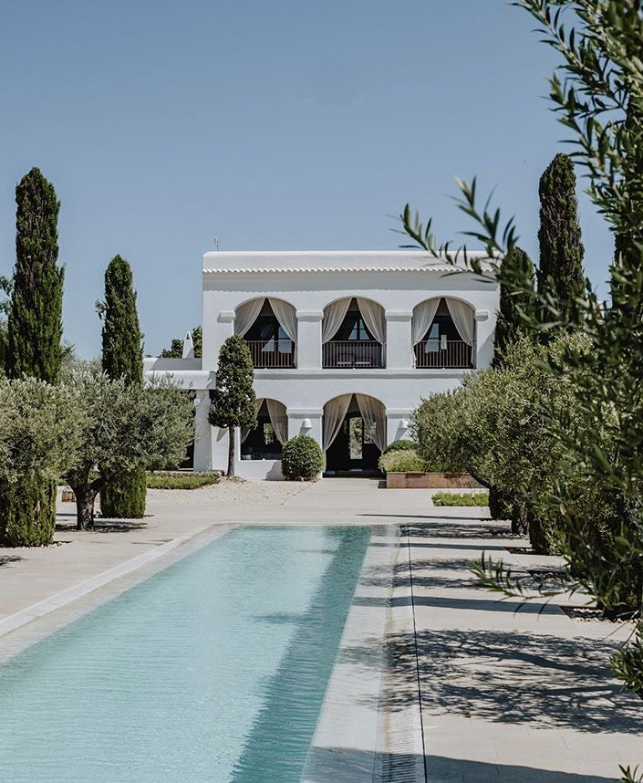 Elegant white-walled boutique hotel with minimalist design, surrounded by lush Mediterranean gardens and stone terraces in Ibiza