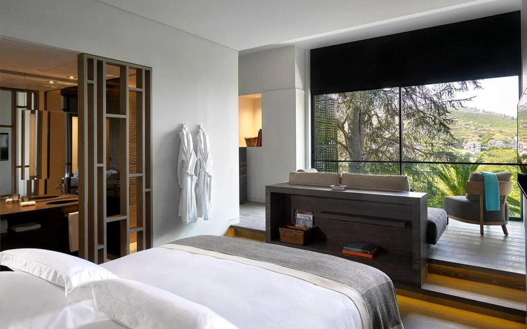 Luxurious modern bedroom with floor-to-ceiling windows overlooking Douro Valley vineyards, featuring a king bed and natural wood accents